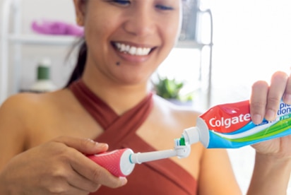 Sieviete smaidot uzspiež Colgate zobu pastu uz zobu birstes vannas istabā.